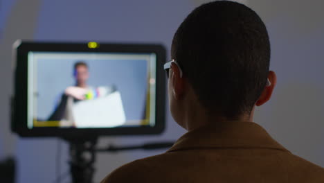 Rear-View-Of-Female-Film-Director-Watching-Performance-Of-Male-Actor-On-Monitor-Shooting-Movie-Or-Video-In-Studio